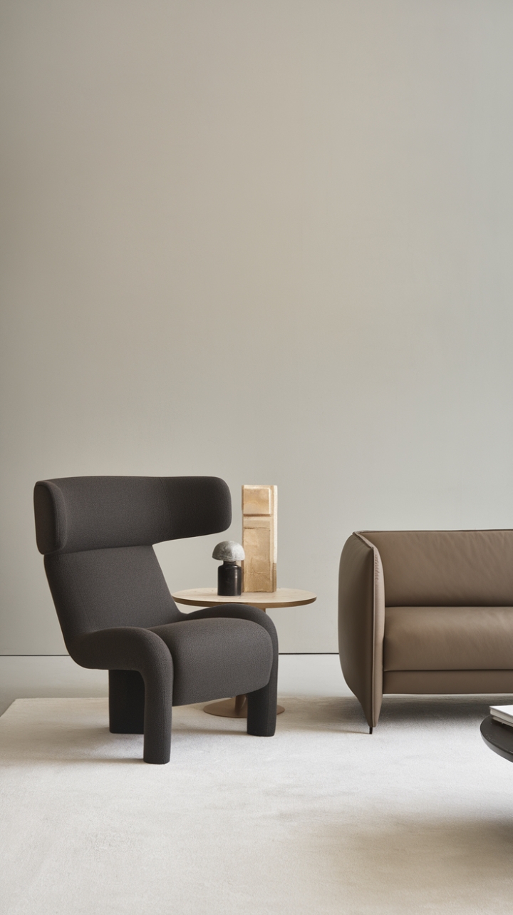 Modernity meets serenity in this impeccably styled living room. A sleek beige sofa anchors the space, its clean silhouette balanced by the fluid grace of a dark grey lounge chair. Subtle contrasts and a calming color scheme create an atmosphere of quiet sophistication, perfect for relaxation and refined living.