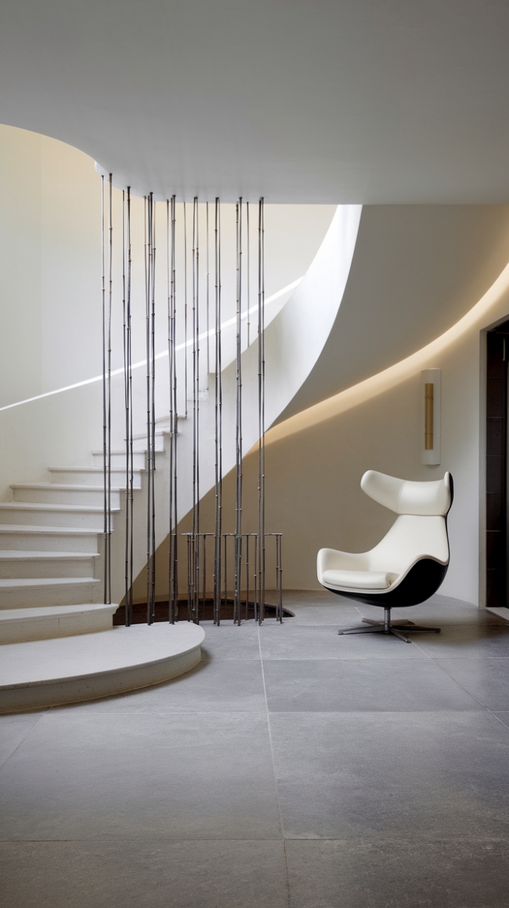 Sculptural curves and minimalist lines define this breathtaking foyer. A pristine white staircase, its form softened by a gentle arc and contrasted by slender black metal railings, anchors the space. Large grey tiles ground the design, while a modern white chair adds a touch of unexpected comfort. The overall effect? Pure, sophisticated serenity.
