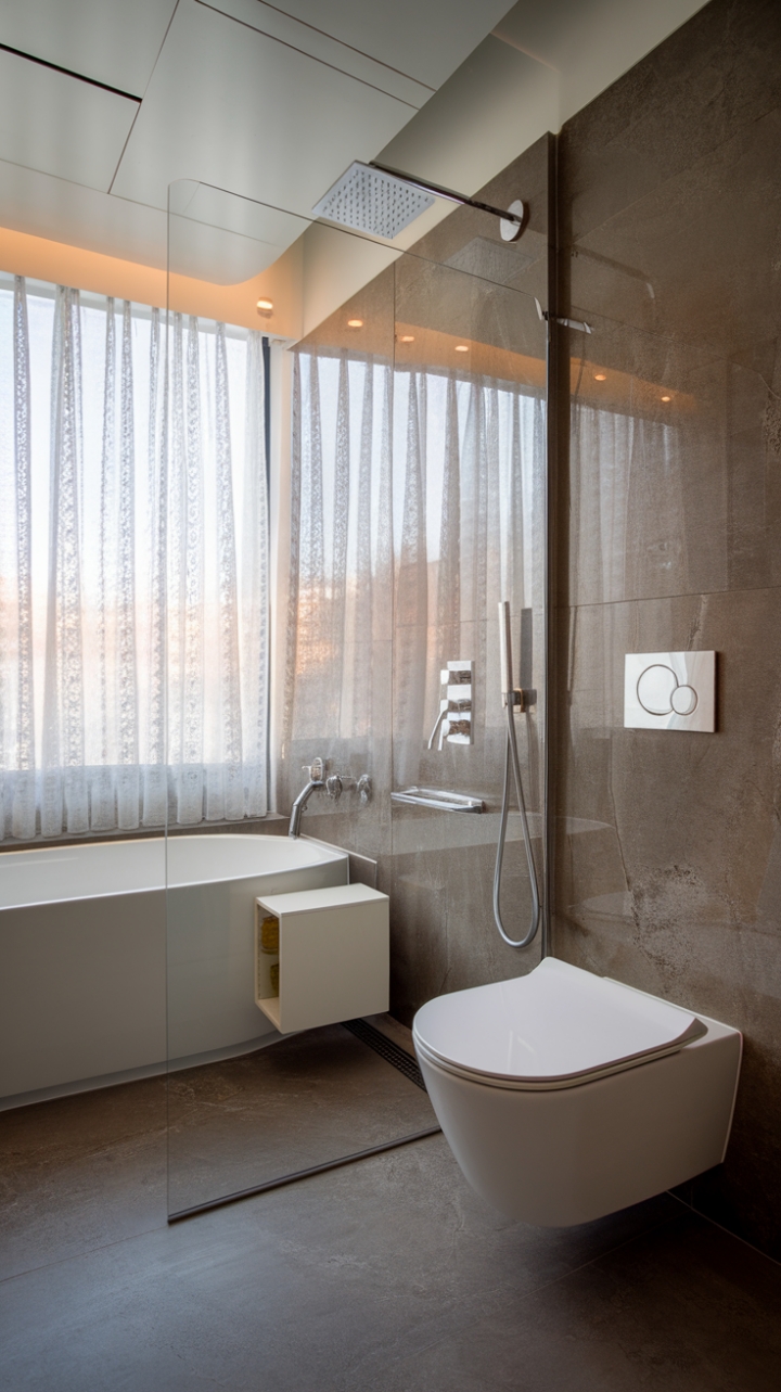 Indulge in the serenity of this contemporary bathroom, where minimalist design meets luxurious comfort. A pristine white tub, rainfall shower, and sleek fixtures create a spa-like sanctuary, while grey tiles and a touch of lace at the window add subtle warmth. The perfect blend of form and function for the modern homeowner.